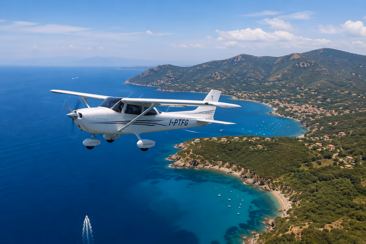 Piccolo aereo bianco in volo sopra una costa mediterranea con mare blu