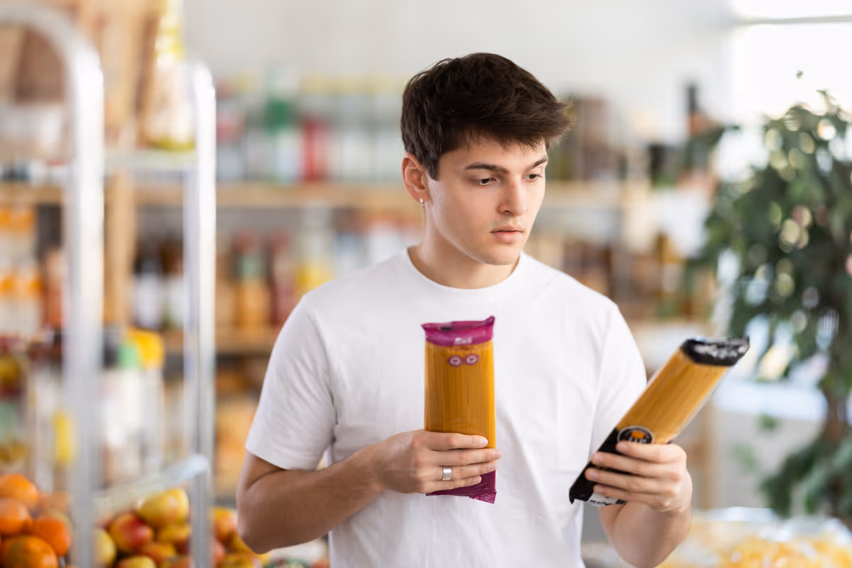 ragazzo in un supermercato che confronta due confezioni di spaghetti leggendone le etichette