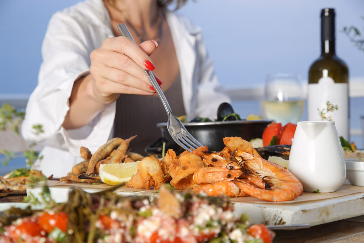 Donna mangia un piatto di pesce fritto con gamberi vicino al mare