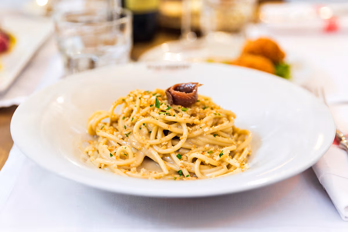 piatto di spaghetti conditi con mollica di pane croccante e un'acciuga sopra