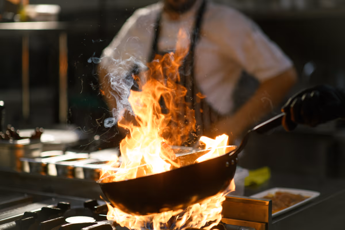 Uno chef in cucina mentre salta ingredienti in padella tra alte fiamme