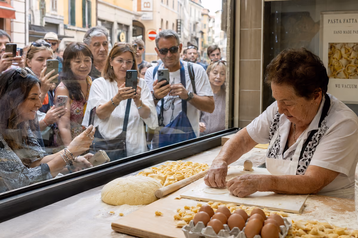 Una signora prepara pasta fresca in vetrina ripresa da turisti con smartphone