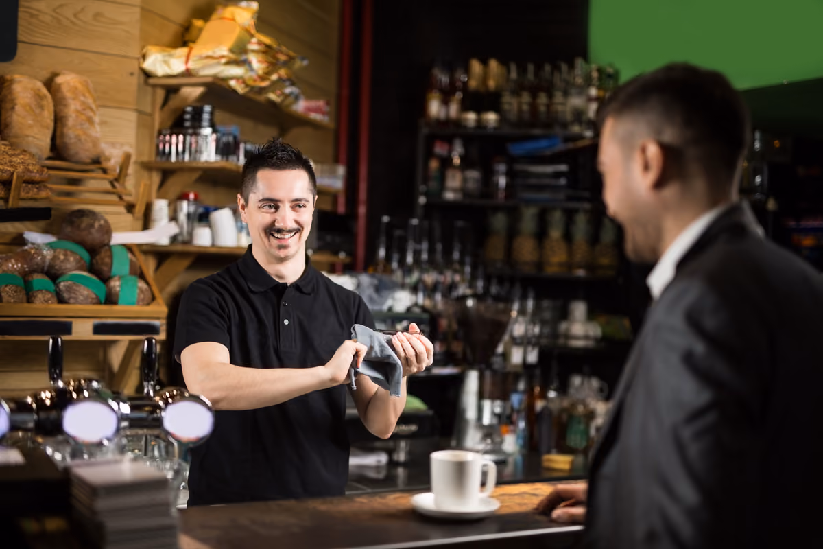 barista sorridente pulisce una tazzina al bancone mentre serve un cliente in giacca