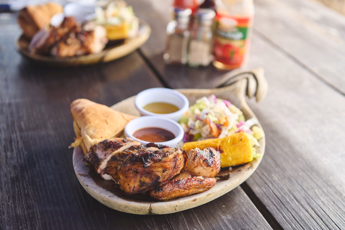Un piatto di jerk chicken servito con contorni tradizionali, salse piccanti e festival, il tipico pane fritto giamaicano