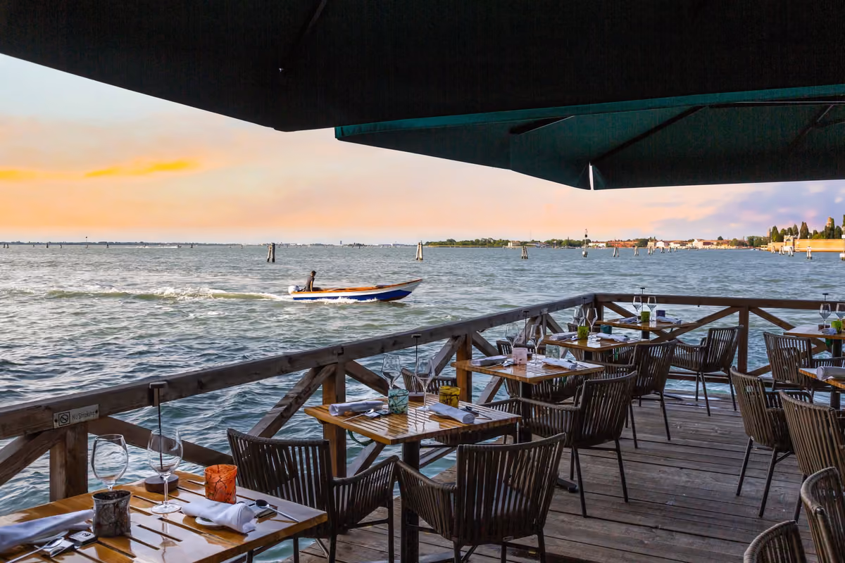 Tavoli apparecchiati su una terrazza in legno affacciata sulla laguna di Venezia al tramonto