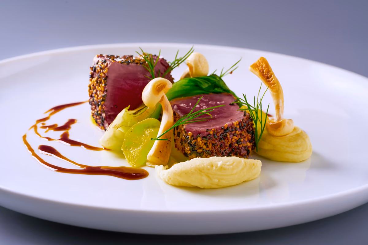 due medaglioni di tonno croccante con funghi purè e salsa scura su piatto