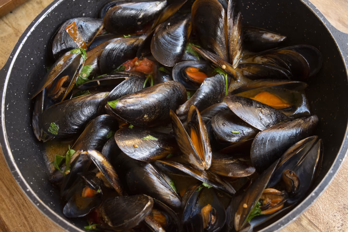 una padella di cozze cotte in un sugo rosso con prezzemolo fresco