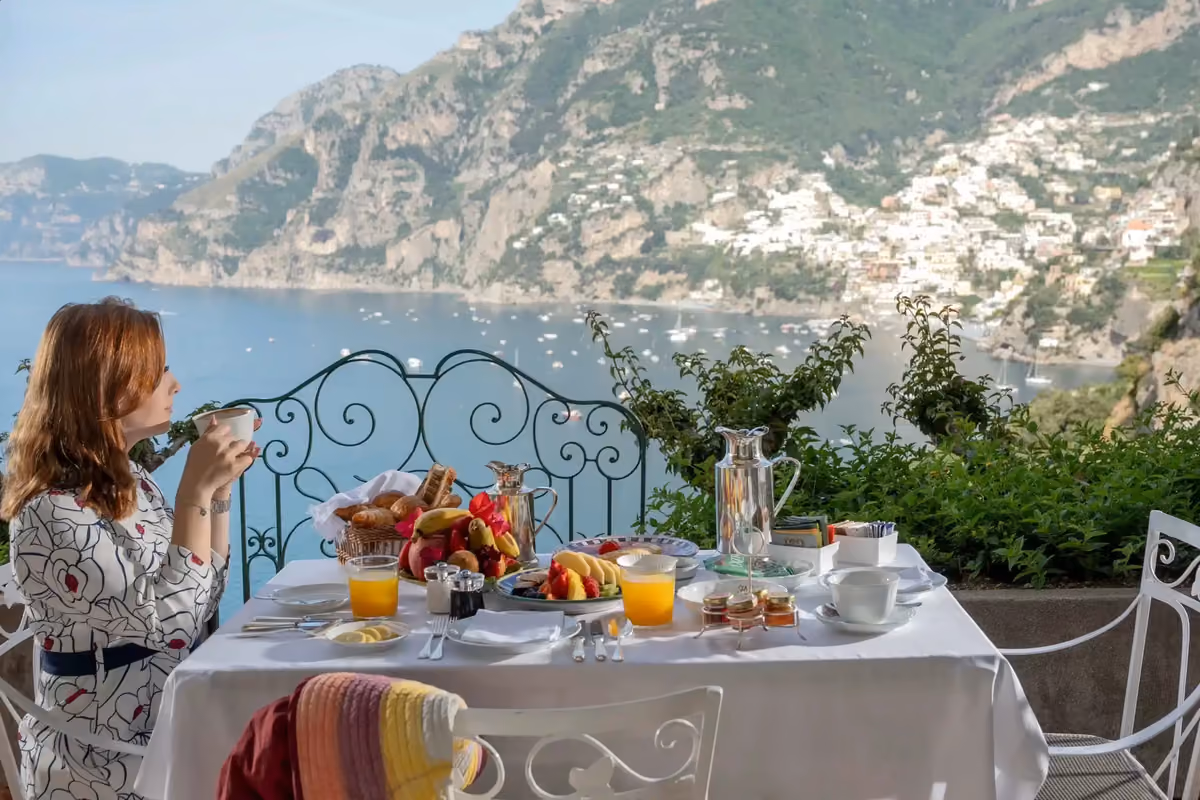 Donna fa colazione su un balcone con vista panoramica sul mare e costa