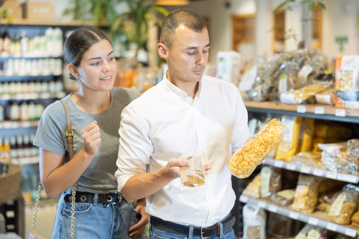 Coppia in un supermercato che esamina con attenzione le etichette di una confezione pasta