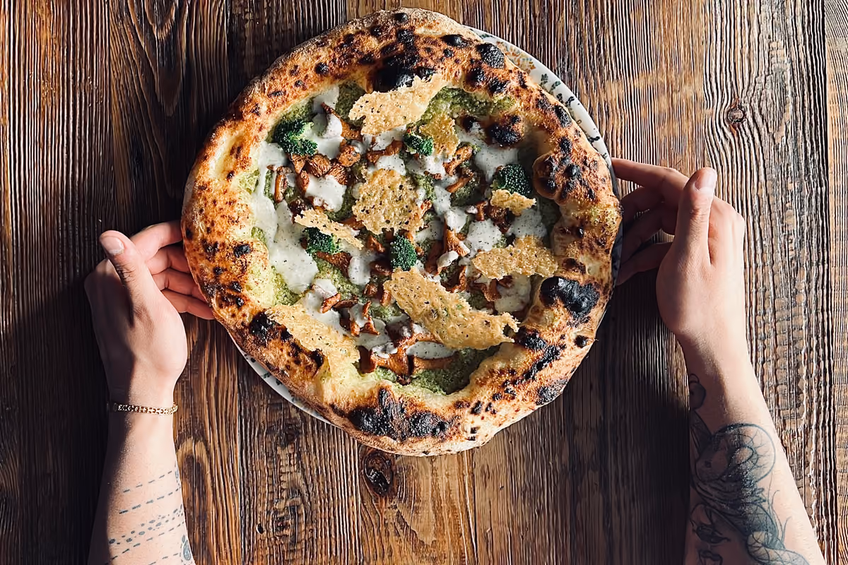 mani che reggono una pizza gourmet guarnita con broccoli funghi e cialde croccanti