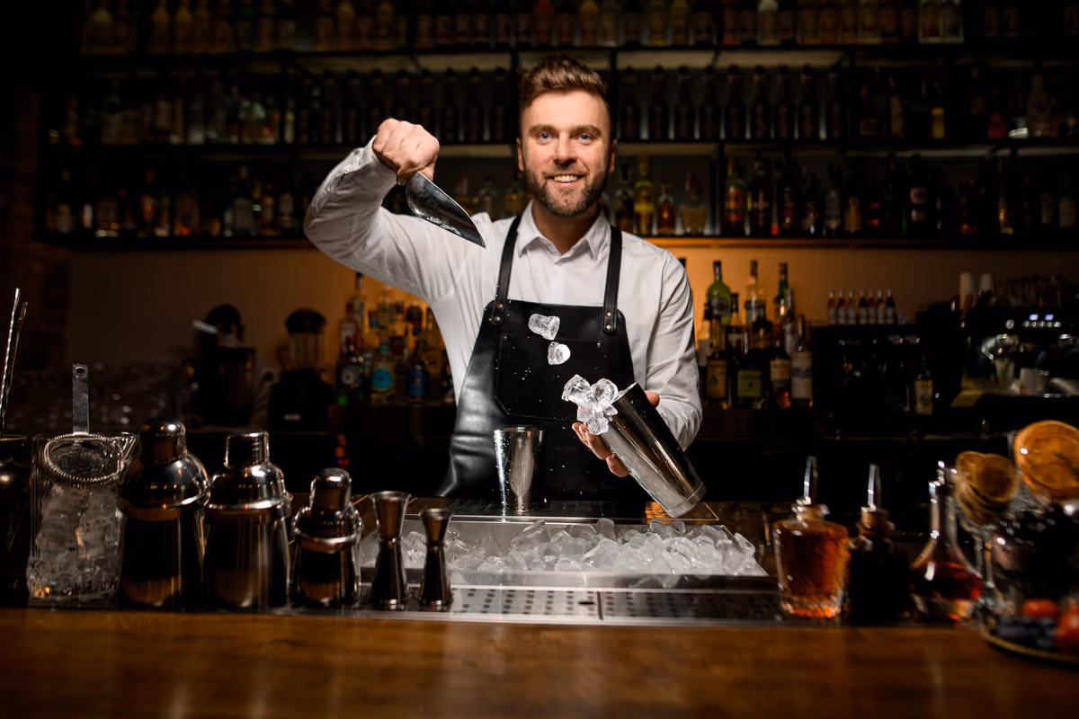 un barman dietro il bancone versa cubetti di ghiaccio nello shaker