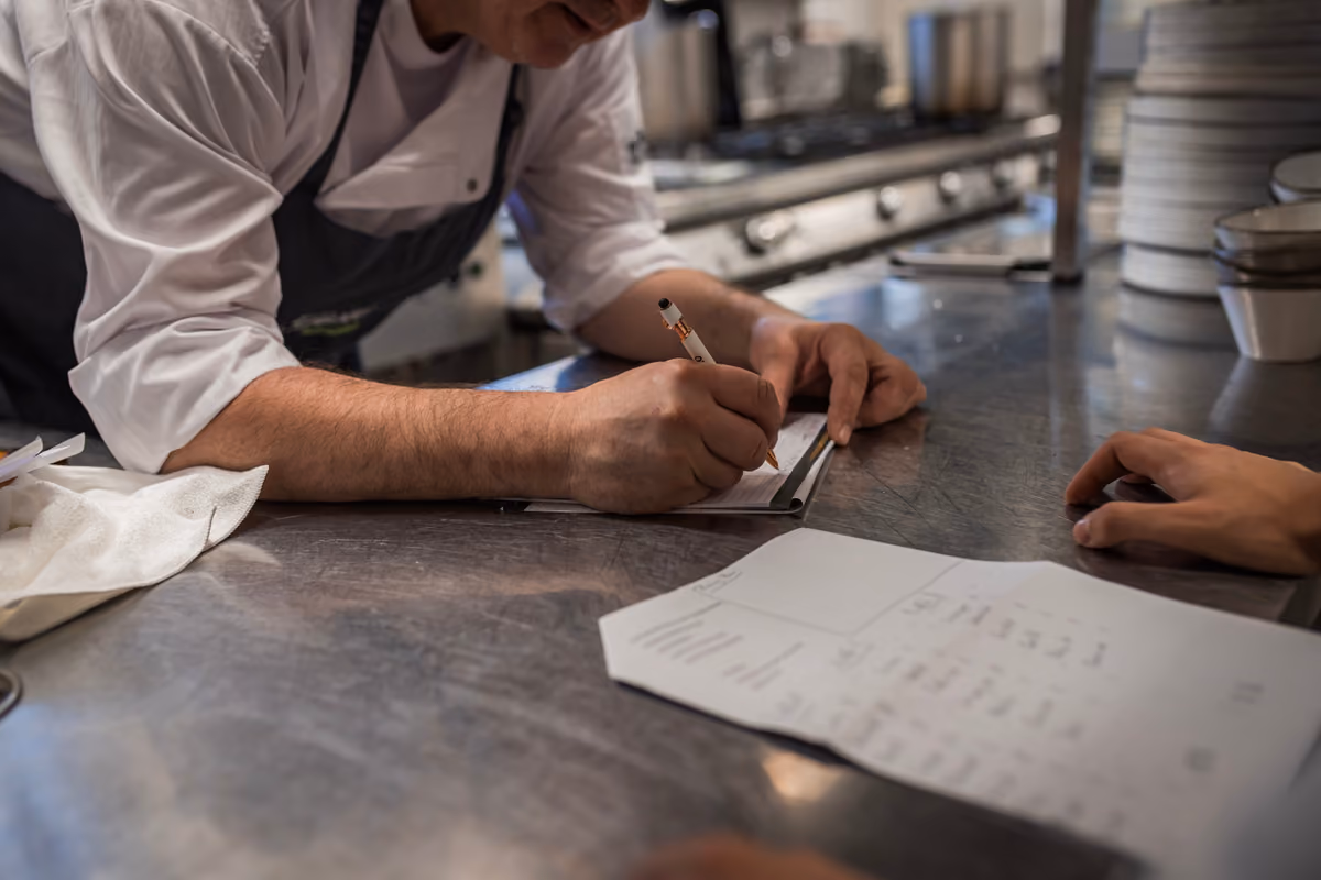 chef scrive su un blocchetto degli ordini su un tavolo di acciaio inox