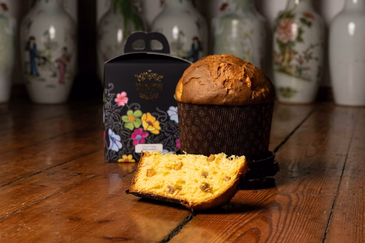 Panettone artigianale accanto alla sua confezione nera con disegni floreali colorati