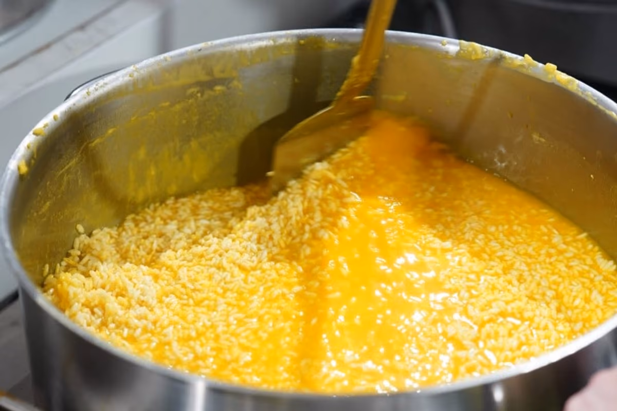 pentola di acciaio inox contenente risotto allo zafferano in cottura mescolato con spatola