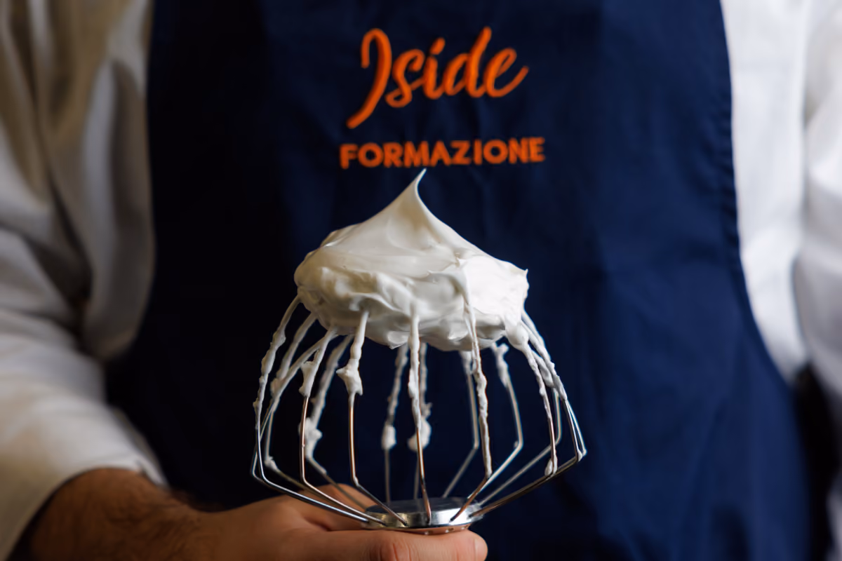 mano di chef con frusta da cucina carica di meringa bianca montata