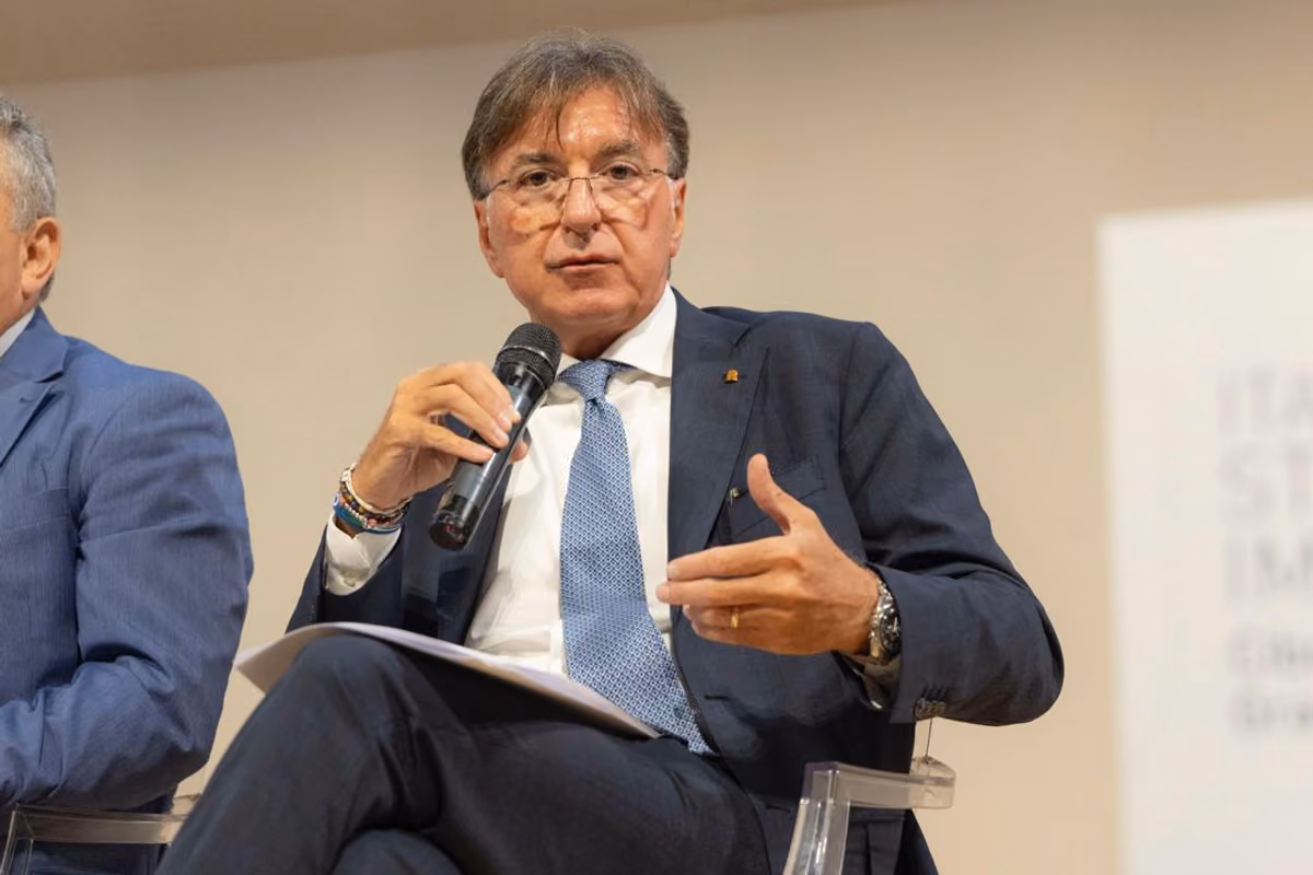 Un relatore in giacca e cravatta parla al microfono durante una conferenza