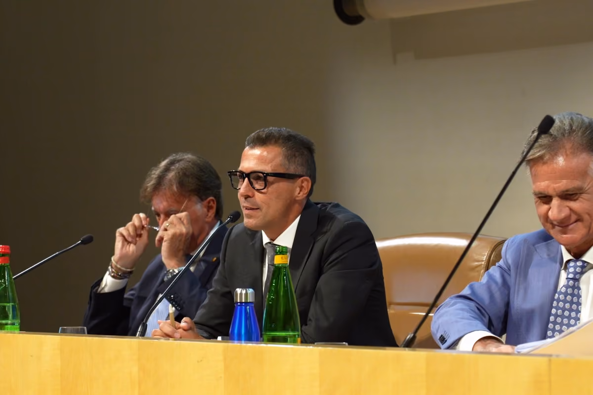 tre uomini seduti al tavolo durante una conferenza con microfoni e bottiglie