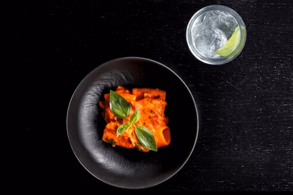 Piatto di pasta al pomodoro con basilico accanto a un bicchiere d'acqua