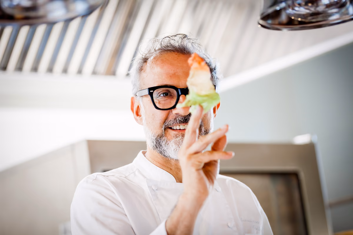 Lo chef Massimo Bottura tiene in mano un piccolo boccone di cibo