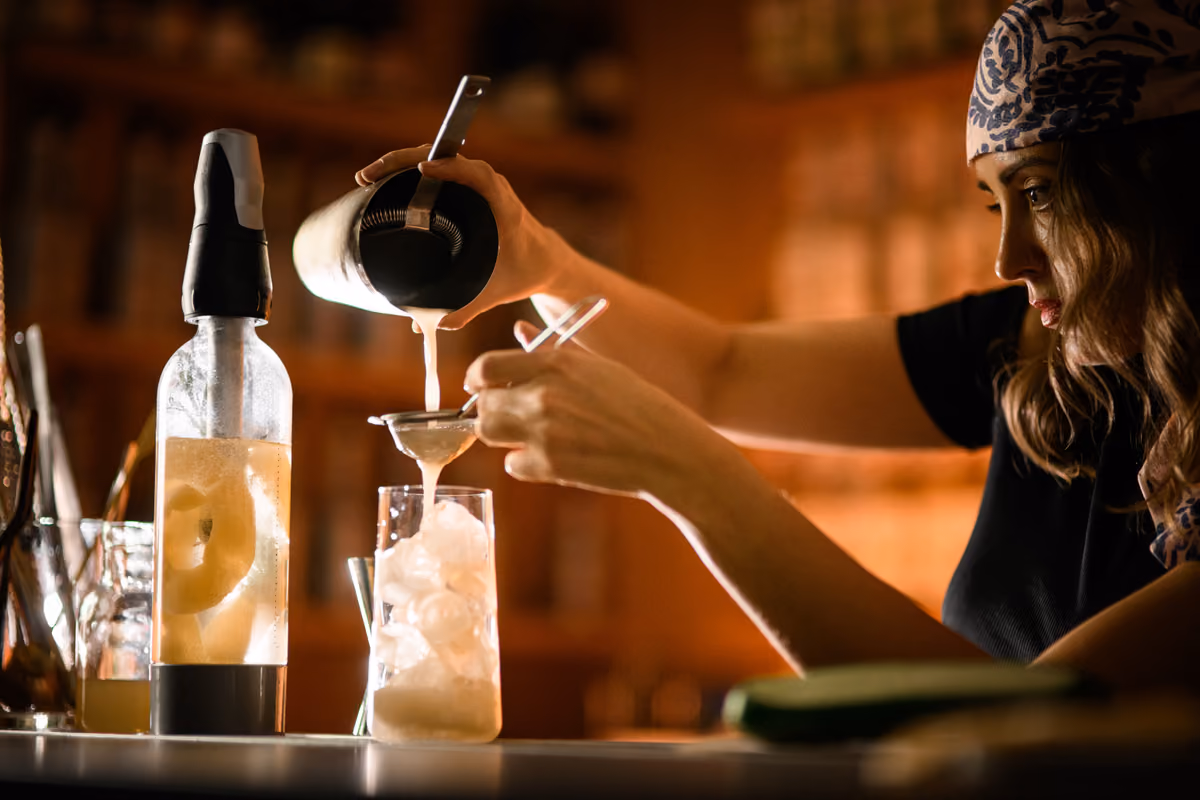 barman prepara un cocktail filtrando il drink in un bicchiere con ghiaccio