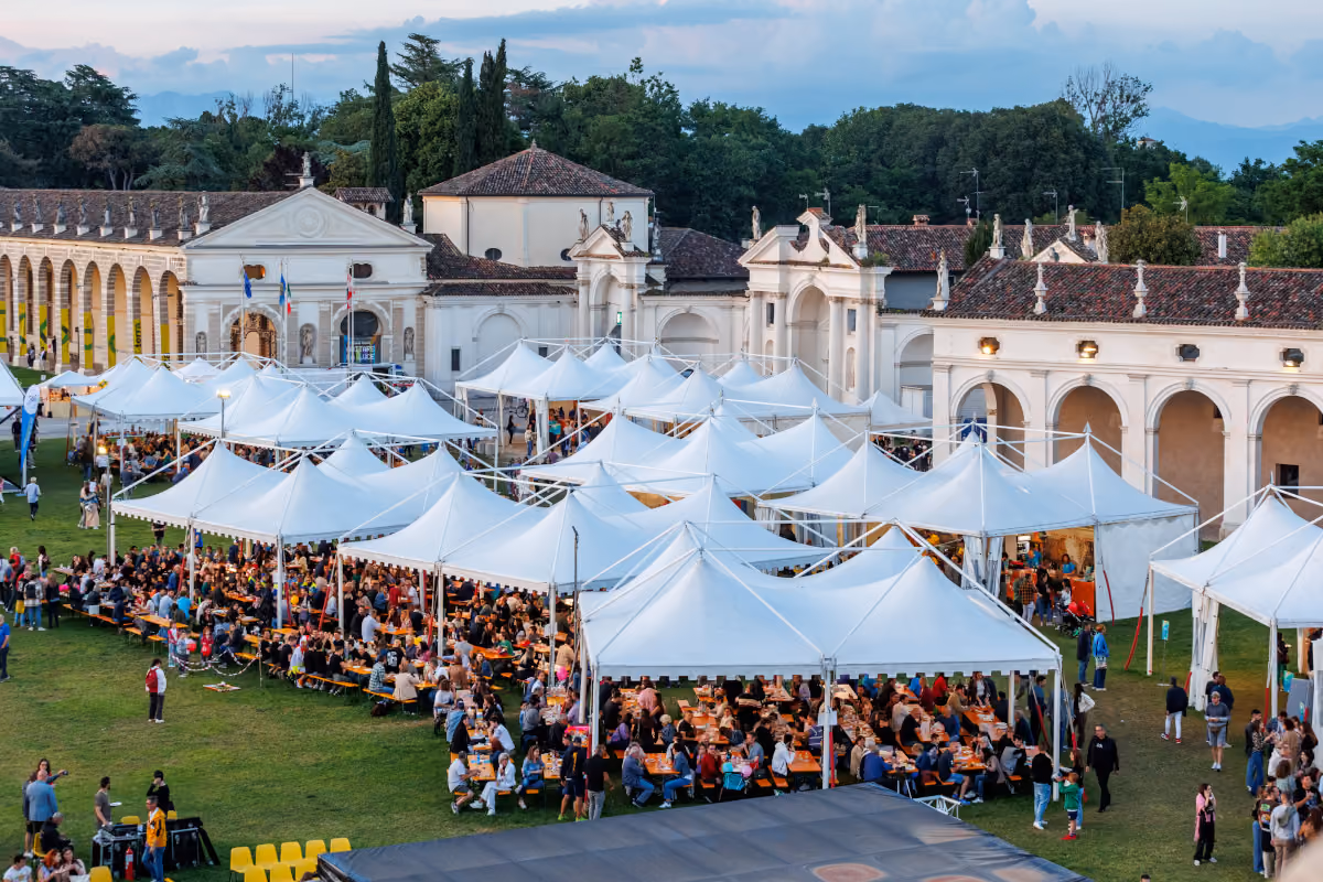 tavolate di persone sotto gazebo bianchi in uno spazio all'aperto davanti a edifici storici