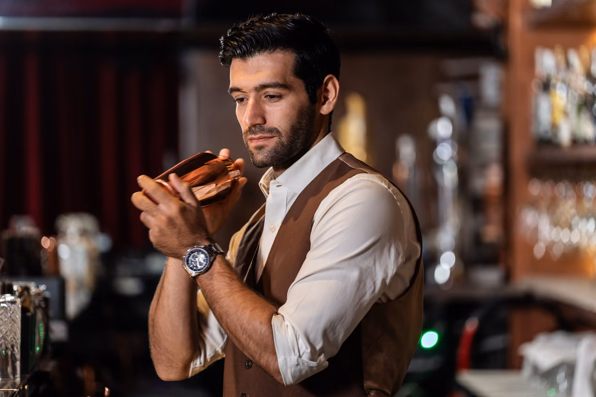 bartender con gilet marrone agita uno shaker in un locale
