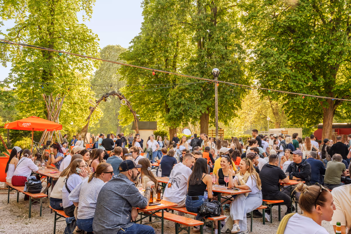Pomeriggio di sole in un tipico Biergarten lungo le rive del fiume, tra alberi e tavoli in condivisione
