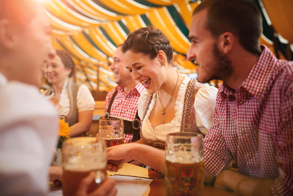 Giovani ridono e brindano con boccali di birra in una tenda tradizionale