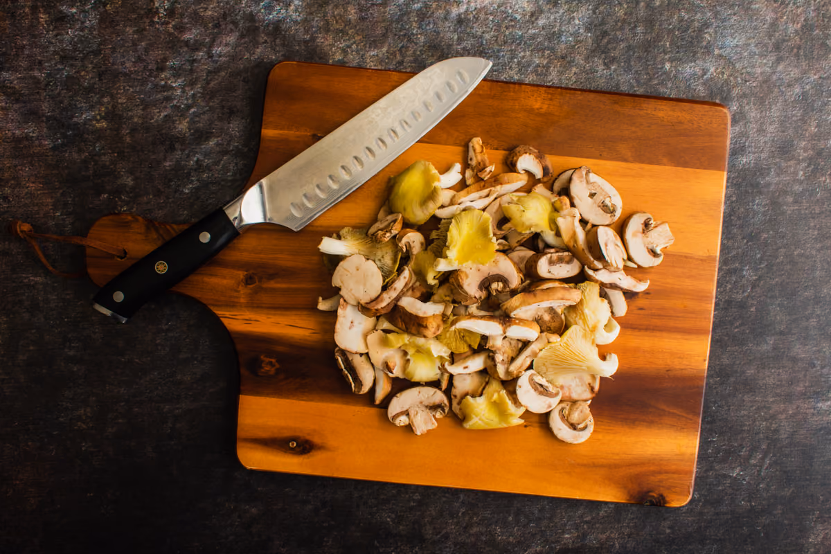 coltello da cucina appoggiato su tagliere in legno con funghi affettati misti