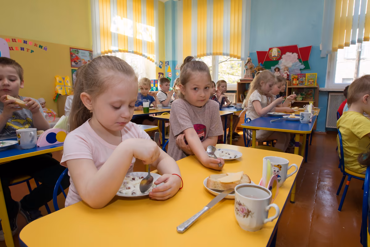 Bambini seduti ai tavoli di una mensa scolastica mentre mangiano la merenda
