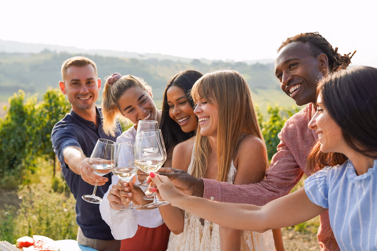 Gruppo di amici brindano con calici di vino bianco tra i vigneti