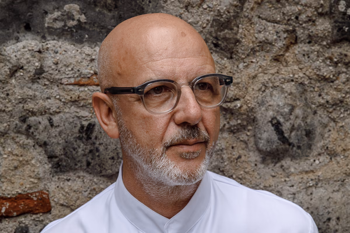 Primo piano dello chef Franco Pepe con occhiali davanti a un muro di pietra