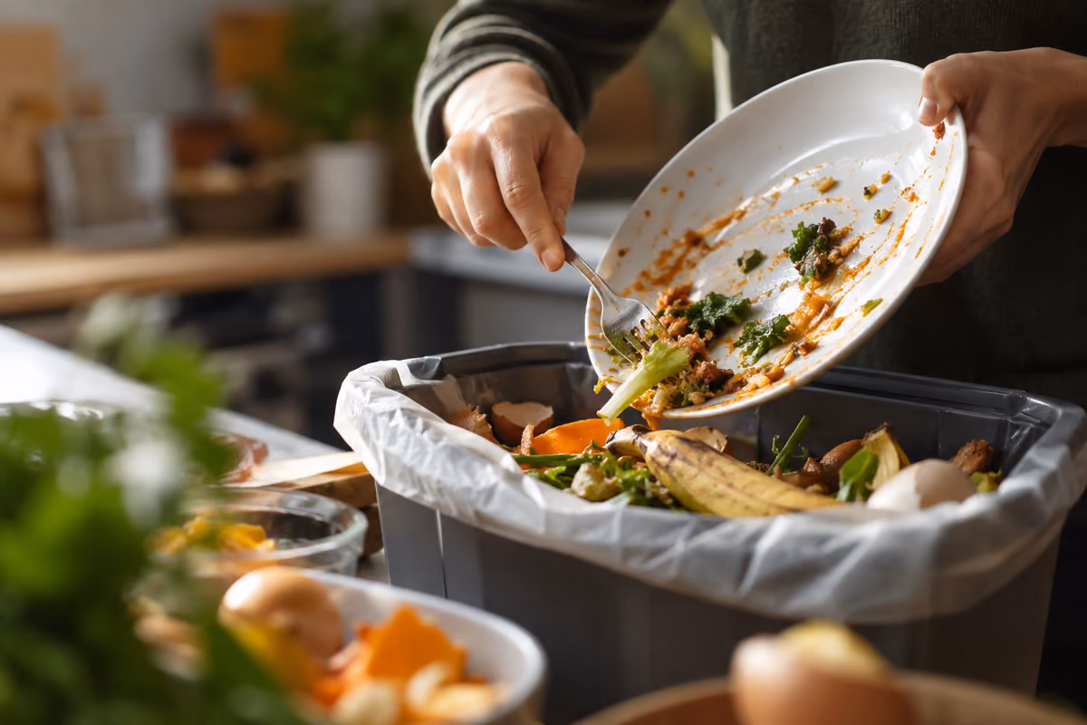 Persona che getta avanzi di cibo dal piatto nel contenitore dei rifiuti organici