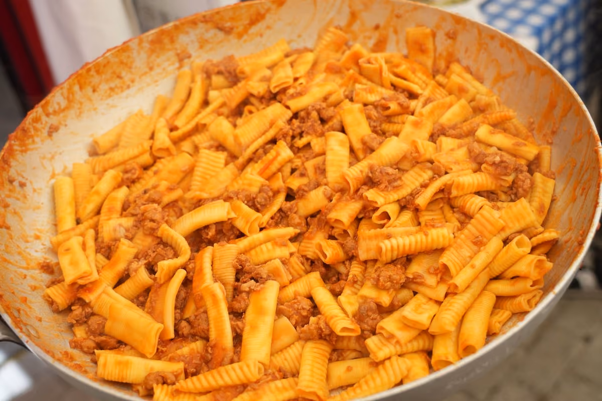 Padella capiente contenente maccheroni al pettine conditi con un ricco ragù di carne