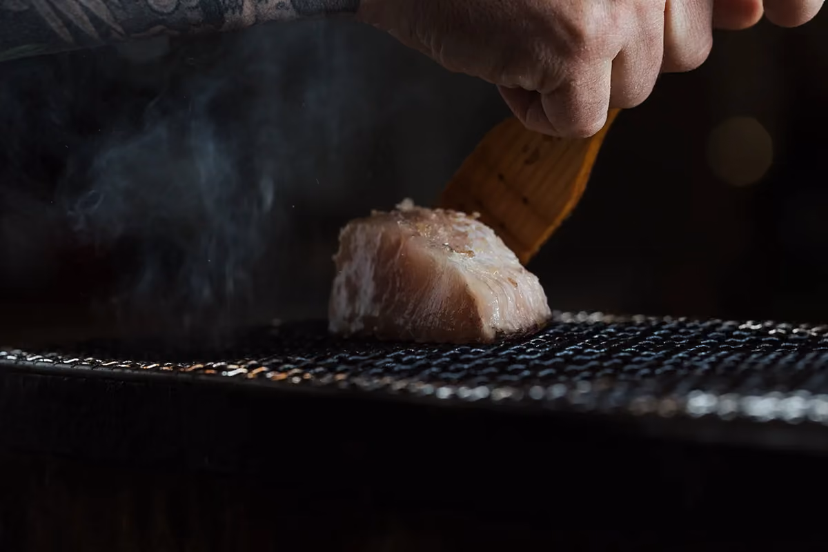 uno chef preme un trancio di pesce fresco sulla griglia fumante