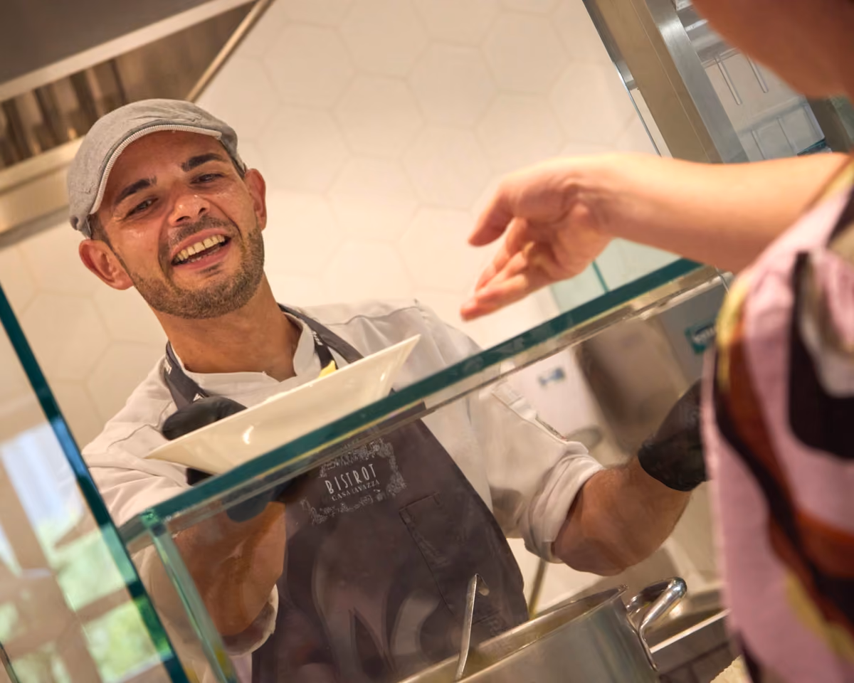 chef sorridente serve un piatto caldo dietro il bancone del Bistrot Lavazza