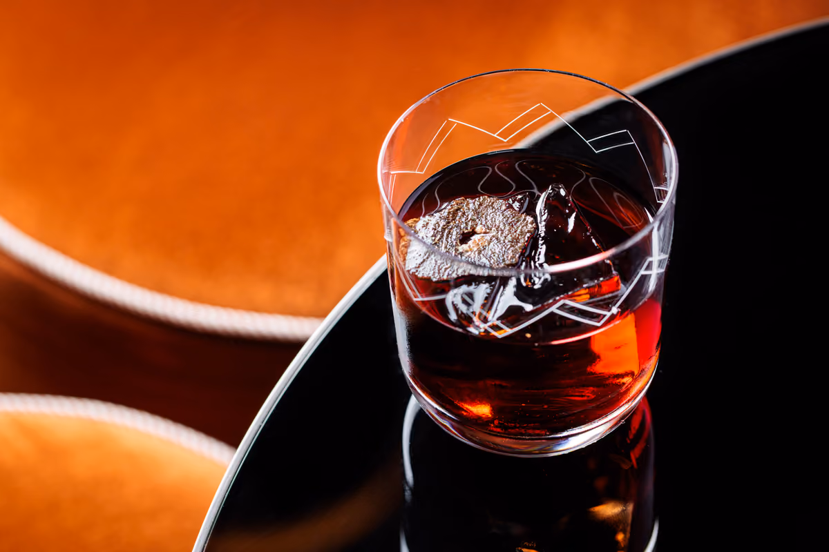 Un bicchiere con cocktail scuro guarnito da una fetta di tartufo