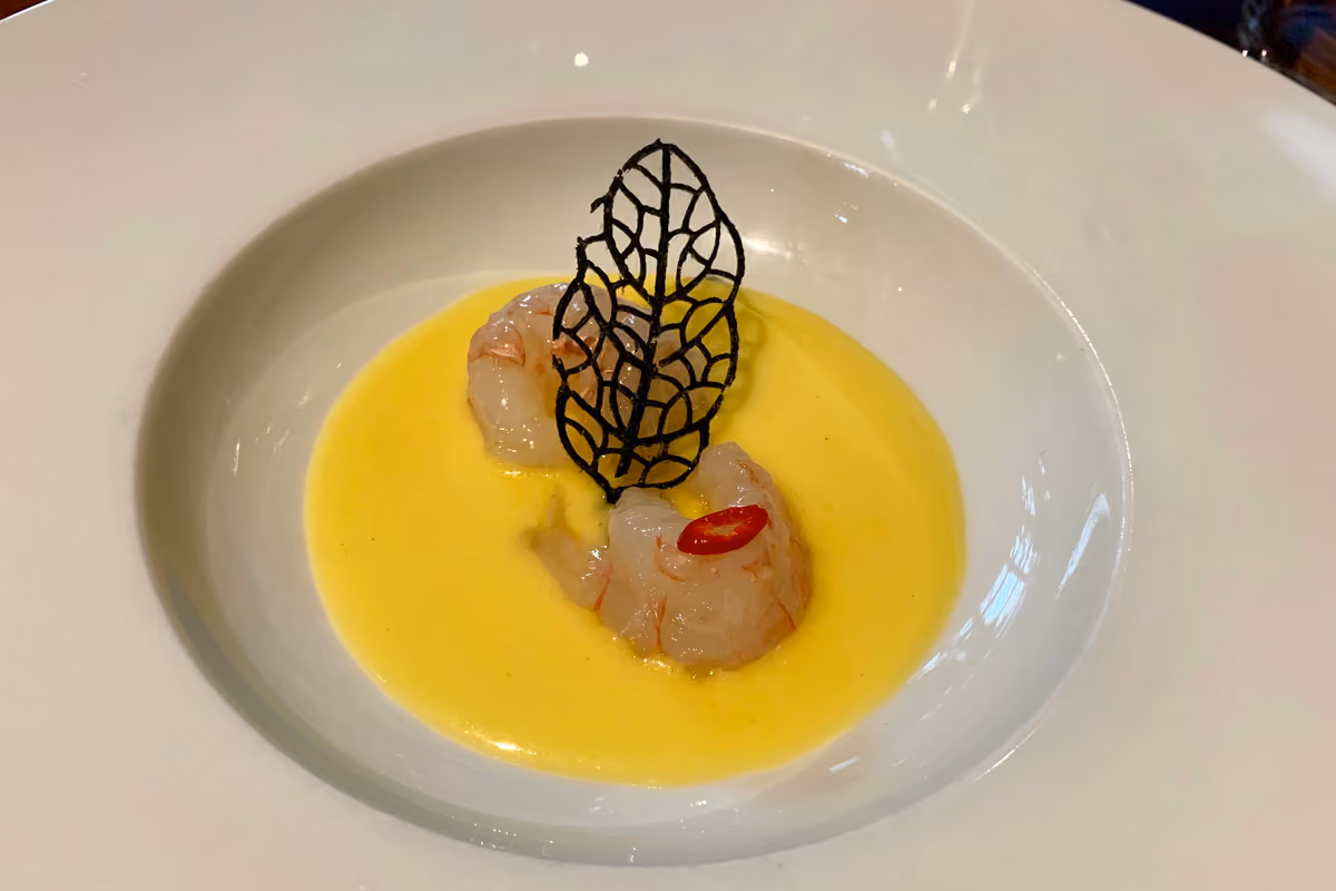 Due gamberi crudi con decorazione nera a foglia in crema gialla nel piatto