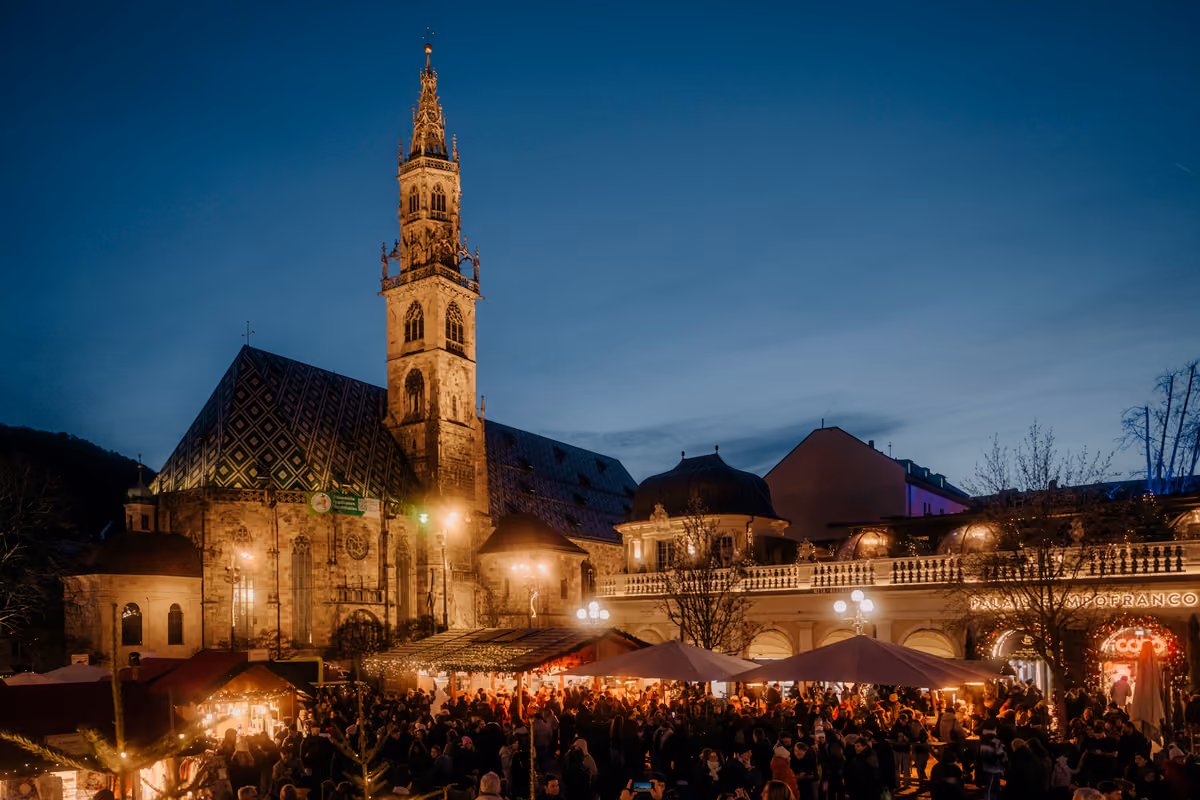 Mercatino di Natale affollato di sera davanti al Duomo di Bolzano
