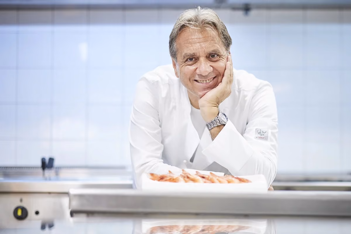 Lo chef Giuseppe Privitera sorride in cucina dietro un vassoio di gamberi crudi