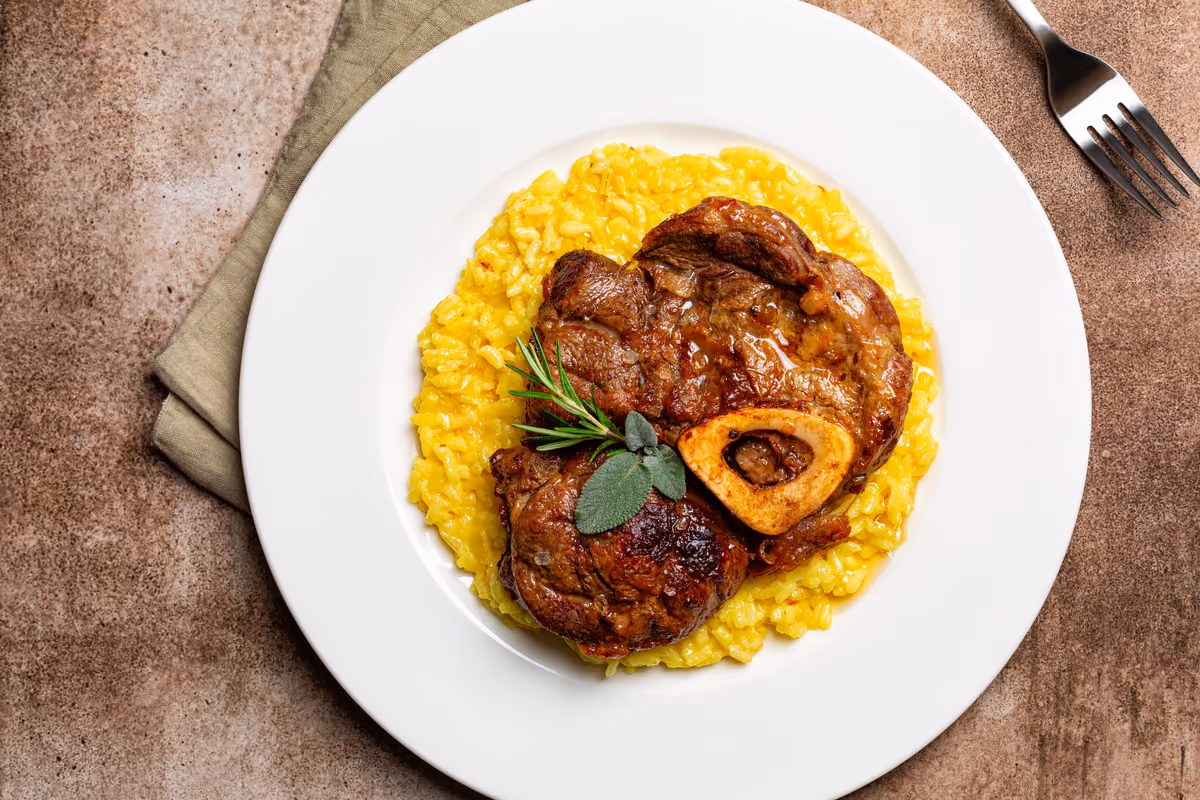 Ossobuco con risotto alla milanese servito su piatto bianco con forchetta