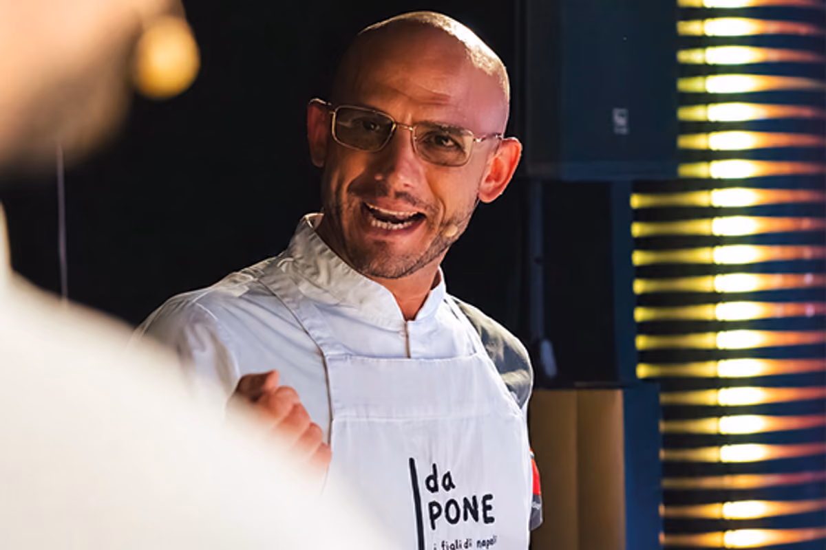 Lo chef Francesco Pone indossa un grembiule bianco in una sala illuminata