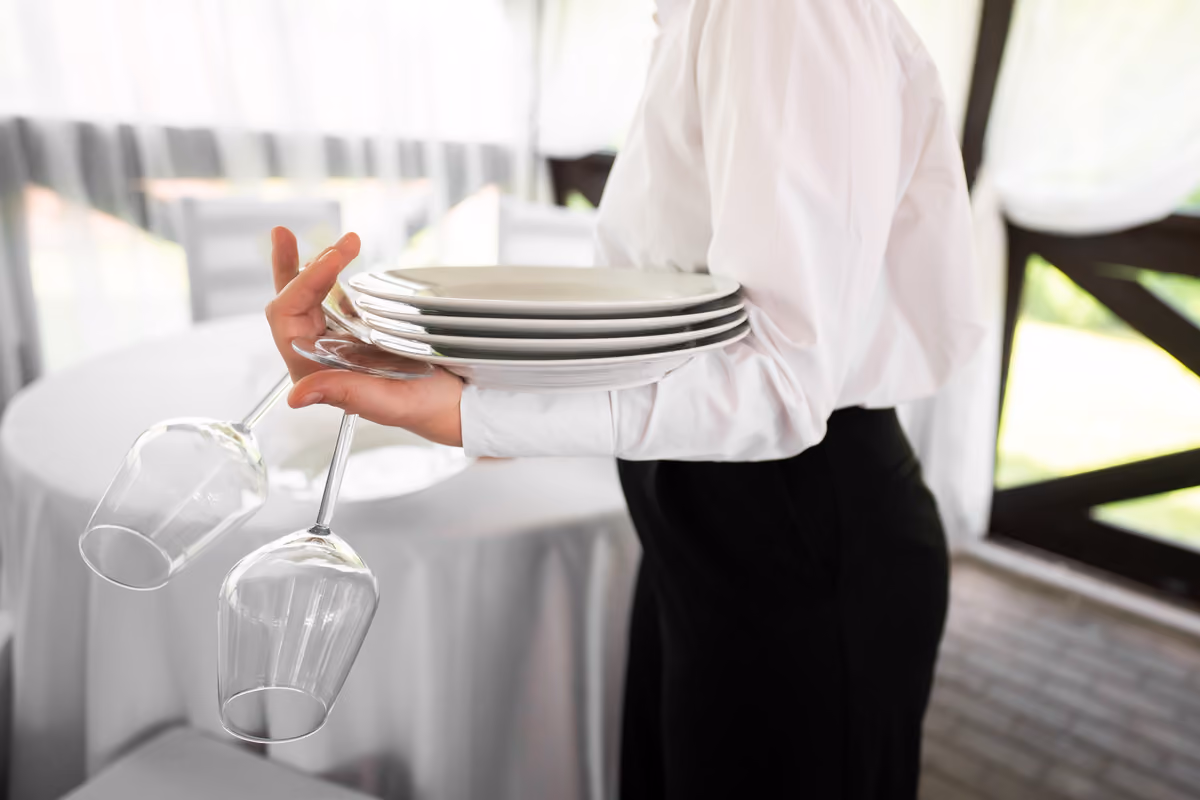 cameriere in divisa che trasporta piatti e calici vuoti in un ristorante