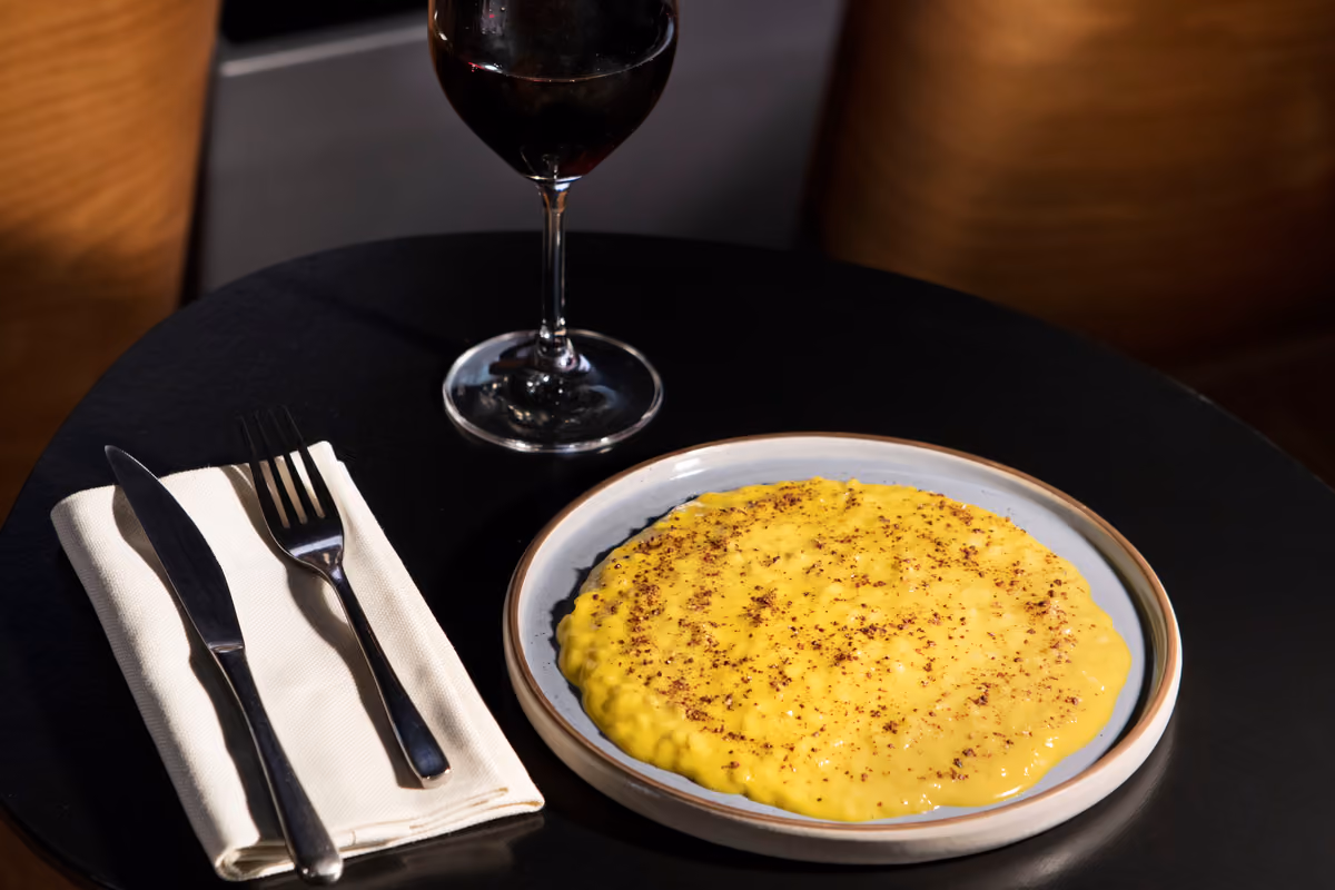 Risotto allo zafferano con spezie su piatto di ceramica, posate e calice di vino