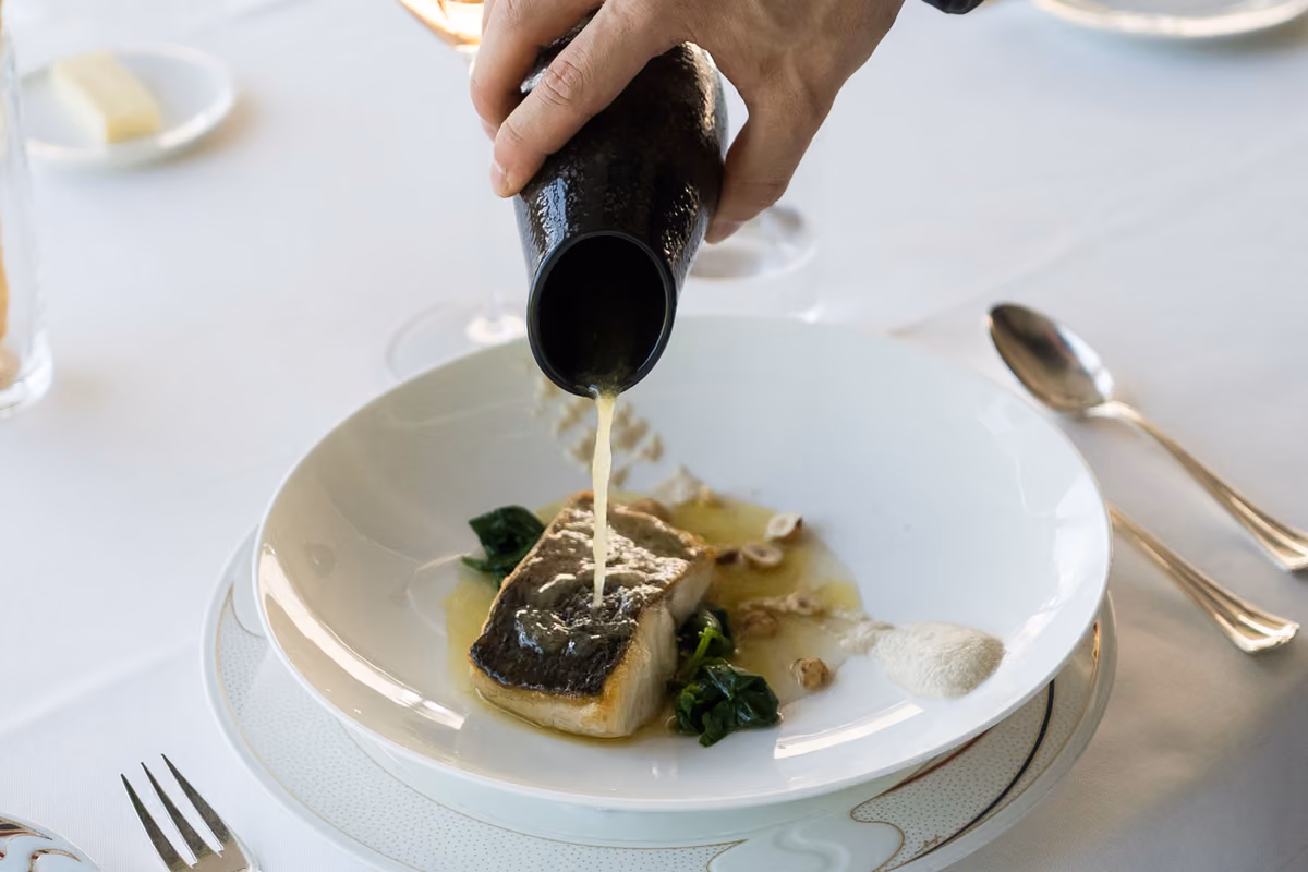 chef versa una salsa su un filetto di pesce cotto in un piatto