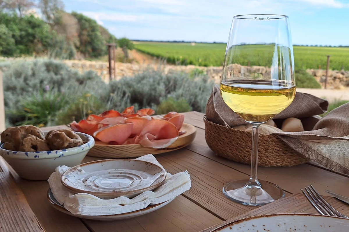bicchiere di vino bianco accanto a un piatto di salumi e pane su tavolo
