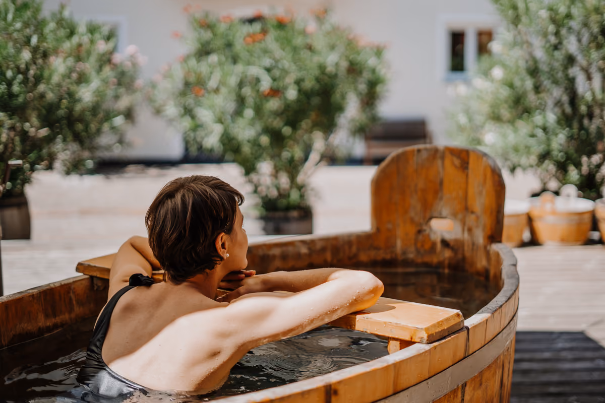 donna rilassata in costume da bagno immersa in una tinozza di legno all'aperto