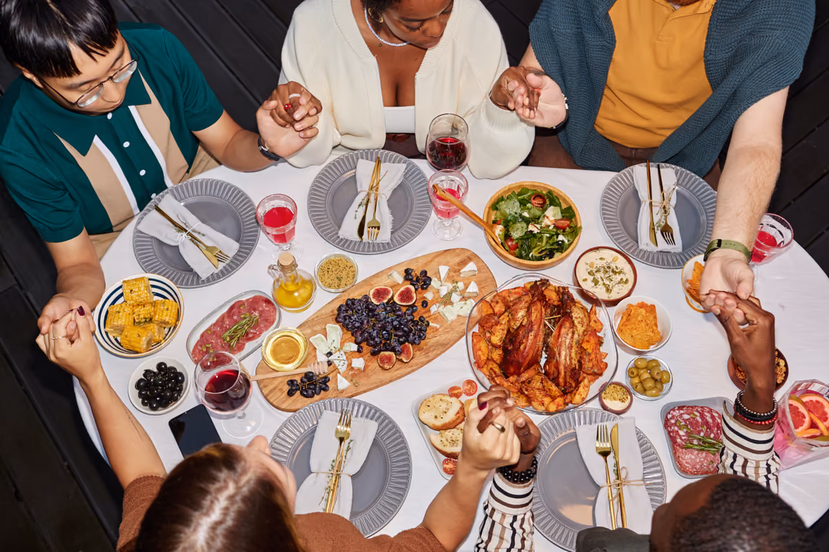 Gruppo di persone sedute a tavola che si tengono per mano prima di mangiare