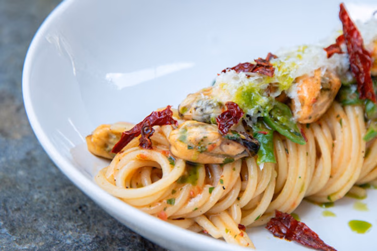 piatto di spaghetti con cozze, pomodori secchi, erbe aromatiche e formaggio grattugiato