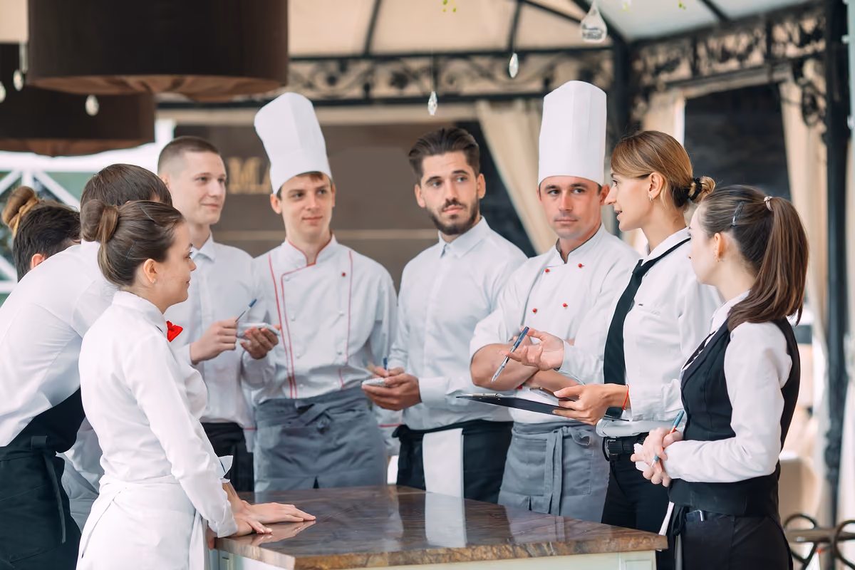 staff di ristorante in uniforme durante una riunione operativa davanti a un tavolo